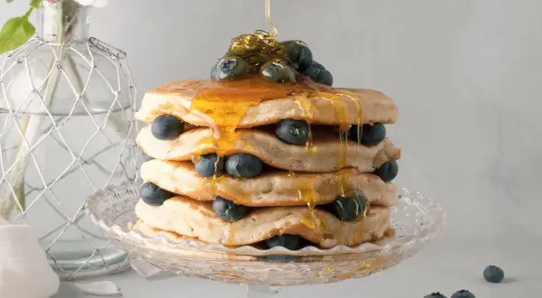 Pancake senza latte, una torre dorata con mirtilli freschi e sciroppo d'acero che cola.
