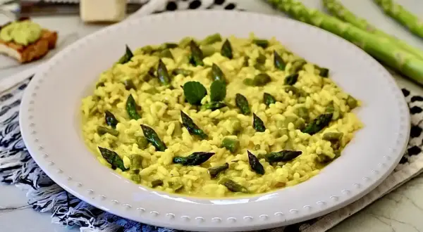 Un cremoso risotto con asparagi, guarnito con punte di asparagi freschi e una fogliolina verde.
