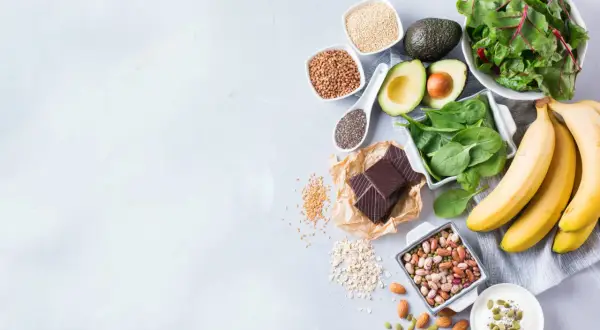 Banane, spinaci, avocado, cioccolato fondente e altri 20 alimenti che alzano la pressione, disposti su un piano grigio.