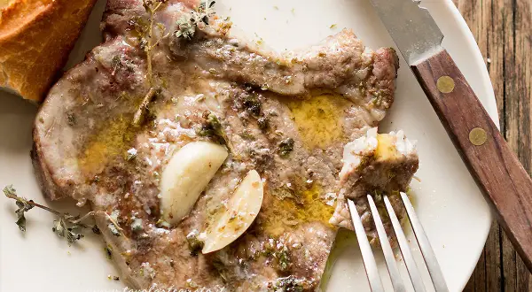 Braciole di maiale succulente, condite con aglio e erbe aromatiche, pronte per essere gustate con pane croccante.