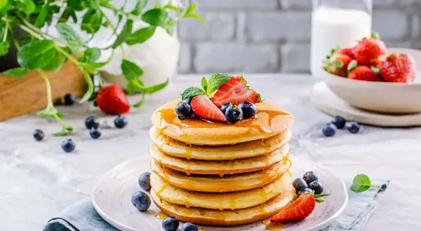 Pila di soffici pancake senza glutine, guarniti con fragole, mirtilli e sciroppo d'acero.