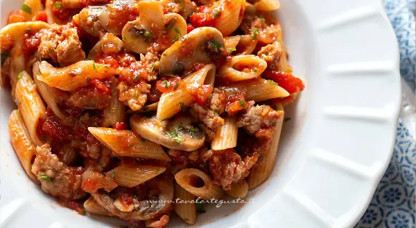 Piatto di pasta alla boscaiola con penne, funghi, salsiccia e pomodoro, condita con prezzemolo fresco.