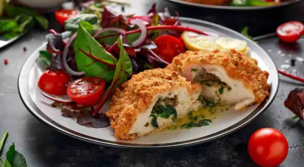 Pollo alla Kiev croccante, ripieno di spinaci e burro, servito con un'insalata fresca di pomodorini e cipolla rossa.
