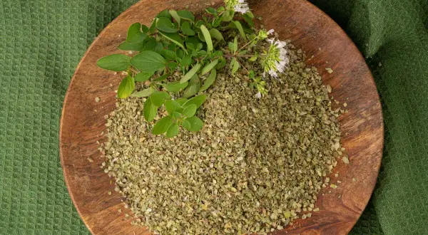 Un piatto di legno con maggiorana essiccata e fresca, pronta per insaporire ogni piatto in cucina.