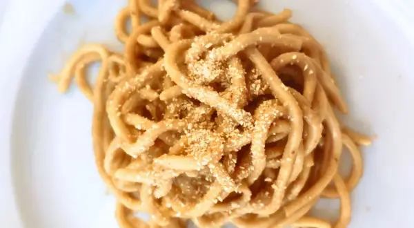 Un piatto di bigoli in salsa, pasta spessa condita con un sugo saporito e cosparsa di pangrattato tostato.