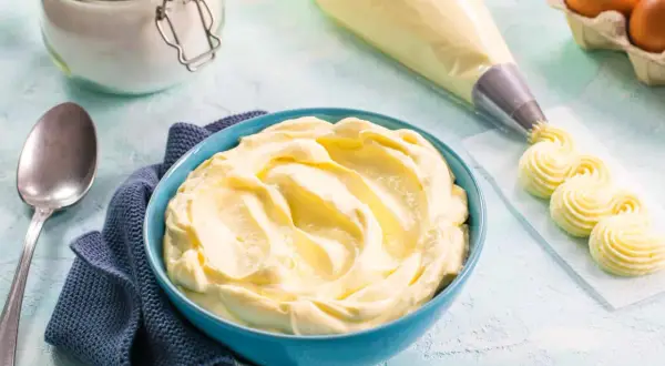 Una ciotola blu piena di soffice crema al mascarpone, pronta per decorare dolci. Accanto, sac à poche e uova.