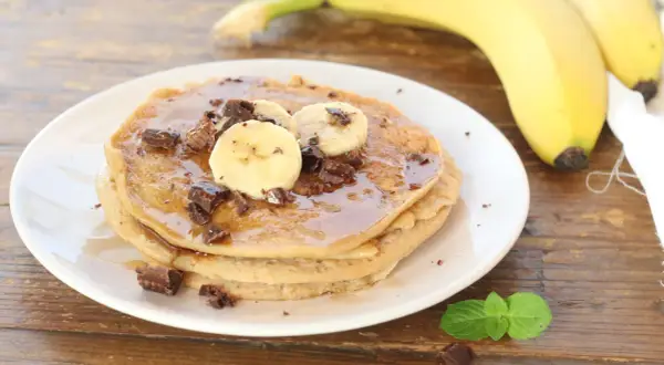 Pancake alla banana con scaglie di cioccolato e sciroppo d'acero, guarniti con fettine di banana fresca.