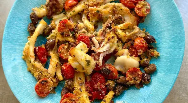 Calamari gratinati al forno con pomodorini e olive, un piatto saporito e croccante servito su un piatto blu.