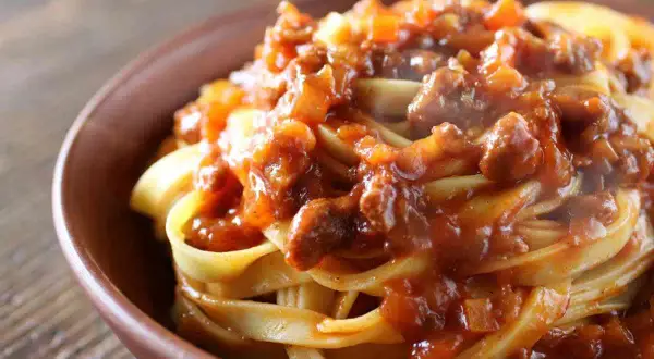 Tagliatelle al ragù, un classico dei primi piatti di carne, servite in una ciotola di terracotta.