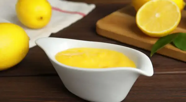 Una ciotola bianca contiene una deliziosa crema al limone, con limoni freschi sullo sfondo.