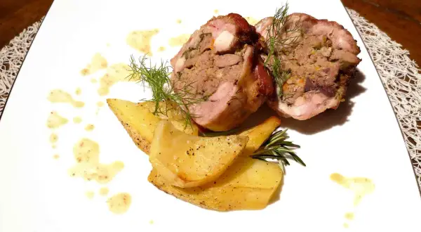 Coniglio in porchetta ripieno, servito con patate arrosto e salsa.