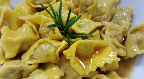 Un piatto invitante di ravioli del plin, conditi con un sugo dorato e guarniti con un rametto di rosmarino fresco.