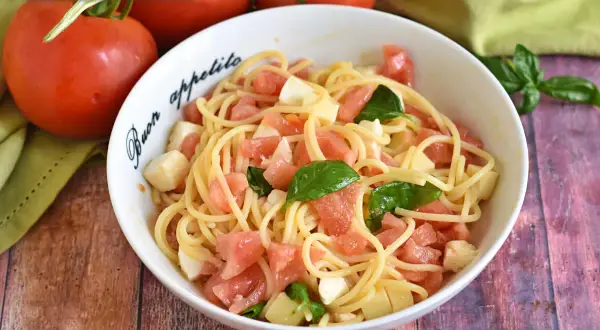 Un piatto di pasta alla checca con pomodori freschi, mozzarella e basilico, pronto per essere gustato.