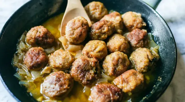 Polpette in bianco succulente in padella con cipolle caramellate, pronte per essere gustate.