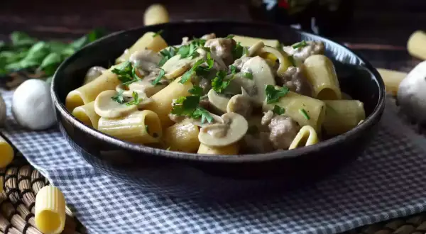 Piatto fumante di pasta con funghi e salsiccia, guarnito con prezzemolo fresco. Un classico confortante.