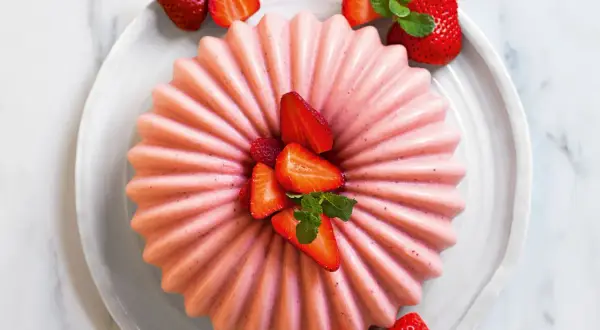 Delizioso bavarese alle fragole, decorato con fragole fresche e menta, su un piatto bianco.