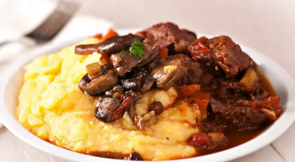 Polenta cremosa con spezzatino di manzo e funghi. Un classico piatto italiano, perfetto per scoprire polenta con cosa accompagnarla.