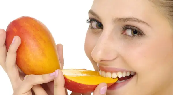 Ragazza sorridente morde un mango succoso, sapendo che il mango è lassativo.