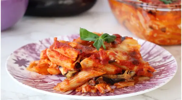 Piatto di pasta alla siciliana con melanzane, pomodoro e formaggio fuso, guarnito con basilico fresco.