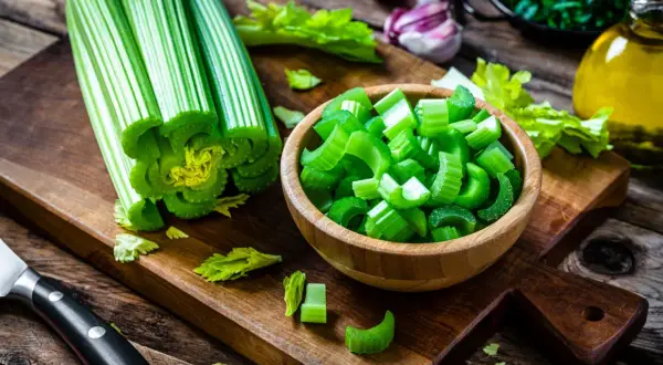 Fresh celery stalks and chopped celery in a wooden bowl on a cutting board.