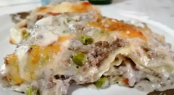 Porzione di lasagne bianche sfiziose con ragù, piselli e besciamella filante, gratinate al forno.