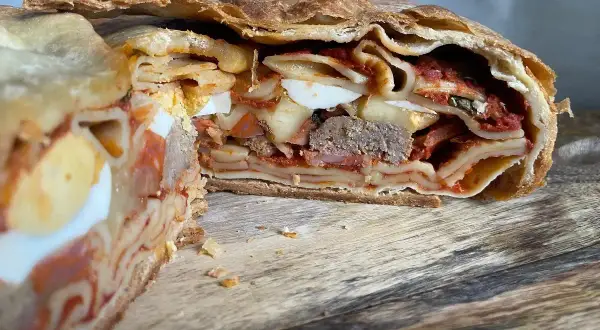 Fetta di timballo di pasta con strati di pasta, uova sode, ragù e carne, racchiuso in una crosta dorata.