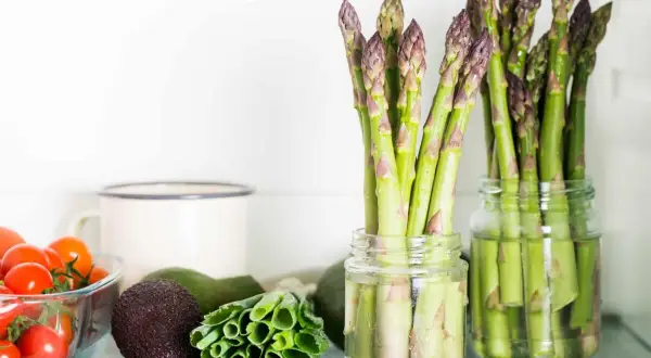 Asparagi freschi in barattoli con acqua, un ottimo modo per conservare gli asparagi. Vicino pomodorini, avocado e cipollotti.