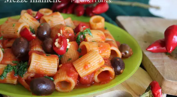 Piatto di pasta mezze maniche con pomodoro, olive e peperoncino, un classico della cucina mediterranea.