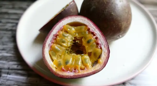Un frutto della passione tagliato a metà, con la polpa succosa e i semi visibili, su un piatto bianco.
