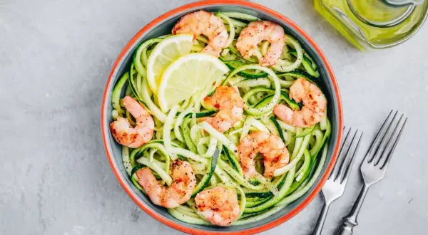 Piatto di spaghetti di zucchine con gamberetti saltati e spicchi di limone. Un modo semplice per imparare come cuocere i gamberetti surgelati.