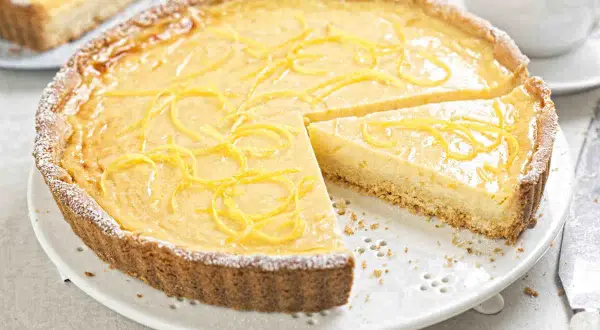 Una deliziosa crostata con crema pasticcera, guarnita con scorza di limone e spolverata di zucchero a velo. Perfetta per ogni occasione.