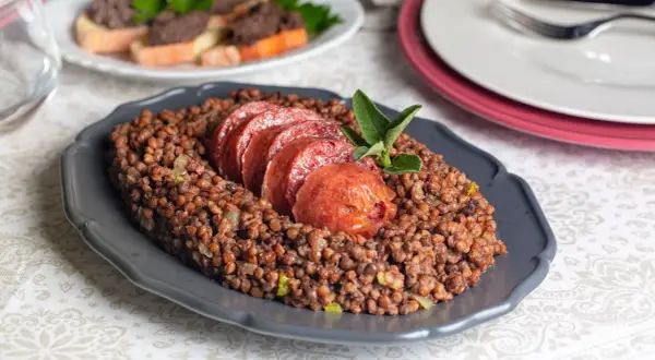 Piatto di lenticchie con fette di cotechino fresco, guarnito con una fogliolina di salvia.