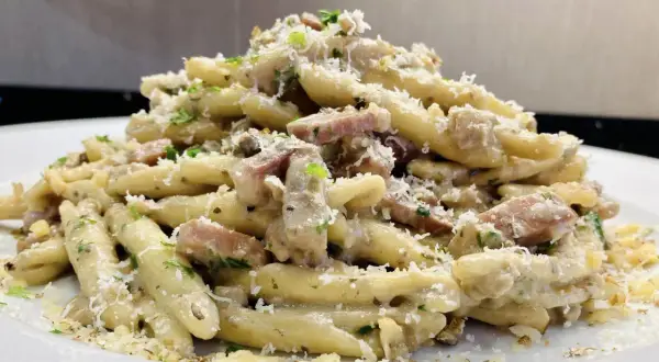 Un piatto invitante di pasta con speck, condita con una cremosa salsa, prezzemolo tritato e abbondante parmigiano grattugiato.