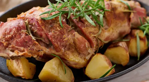 Succulento agnello al forno, dorato e profumato al rosmarino, servito con patate arrosto in una padella di ghisa.