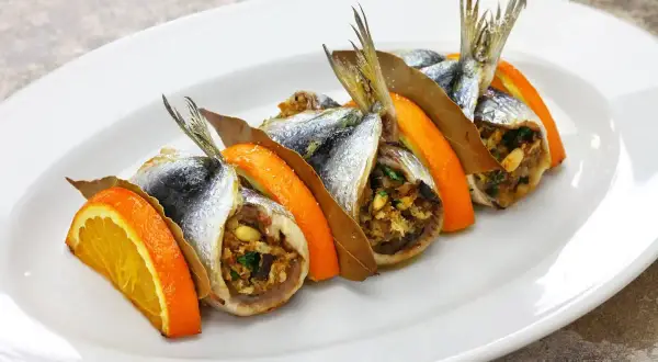 Sarde a beccafico su un piatto bianco, guarnite con fette d'arancia e foglie di alloro. Un piatto tradizionale siciliano.