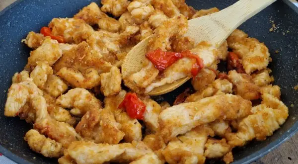 Straccetti di pollo dorati e saporiti in padella con pomodorini, pronti per essere gustati.