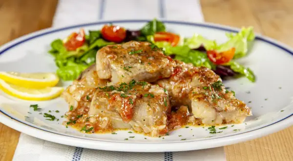 Deliziosi bocconcini di coda di rospo in umido con pomodoro e prezzemolo, accompagnati da insalata fresca e spicchi di limone.