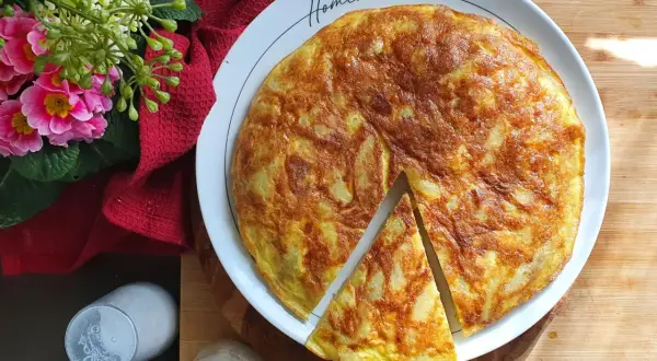 Una deliziosa frittata di patate fatta in casa, dorata e invitante, servita su un piatto bianco con fiori rosa e un tovagliolo rosso.
