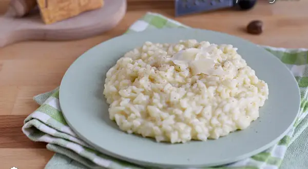 Un cremoso risotto alla parmigiana, guarnito con scaglie di formaggio, pronto per essere gustato.