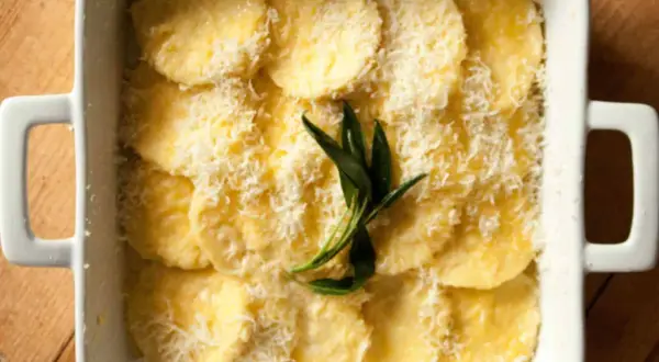 Gnocchi alla Romana pronti per essere infornati, conditi con parmigiano grattugiato e un rametto di salvia.