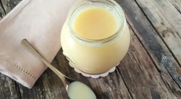 Un vasetto di latte condensato fatto in casa, denso e cremoso, pronto per dolci deliziosi. Un cucchiaino ne mostra la consistenza perfetta.