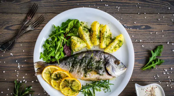 Orata in padella, cotta alla perfezione, servita con patate, limone e insalata fresca. Un piatto delizioso e salutare.