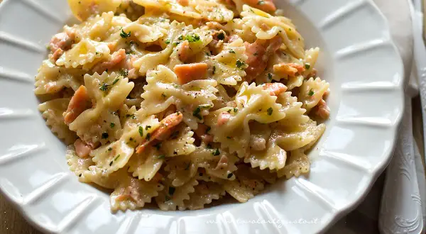 Farfalle cremose con pezzetti di salmone e prezzemolo tritato, un piatto invitante di pasta al salmone.