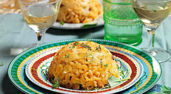 Anelletti al forno dorati e invitanti, guarniti con erbe aromatiche, serviti su piatti colorati con bicchieri di vino bianco.