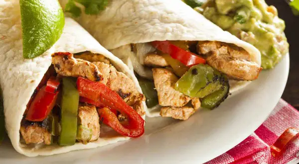 Due fajitas di pollo con peperoni, cipolle e guacamole. Un piatto saporito e colorato, pronto per essere gustato.