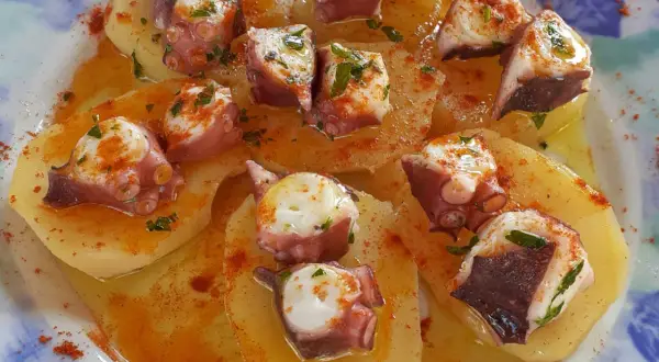 Un delizioso polpo alla gallega su patate, condito con paprika e prezzemolo, servito su un piatto blu e bianco.
