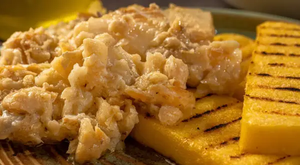 Un saporito baccalà alla vicentina, cremoso e profumato, servito su fette di polenta grigliata.