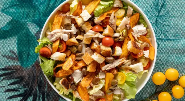Insalata di pollo ricca con crostini, pomodorini, olive e patate dolci croccanti. Un piatto gustoso e colorato.
