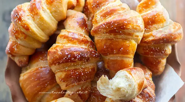 Cornetti fatti in casa dorati e soffici, spolverati di zucchero a velo, invitano a una colazione golosa.