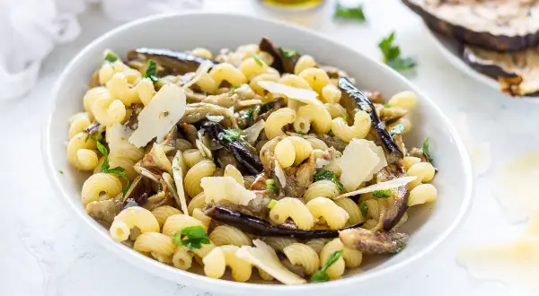 Piatto di pasta con melanzane in bianco, condita con scaglie di parmigiano e prezzemolo fresco.